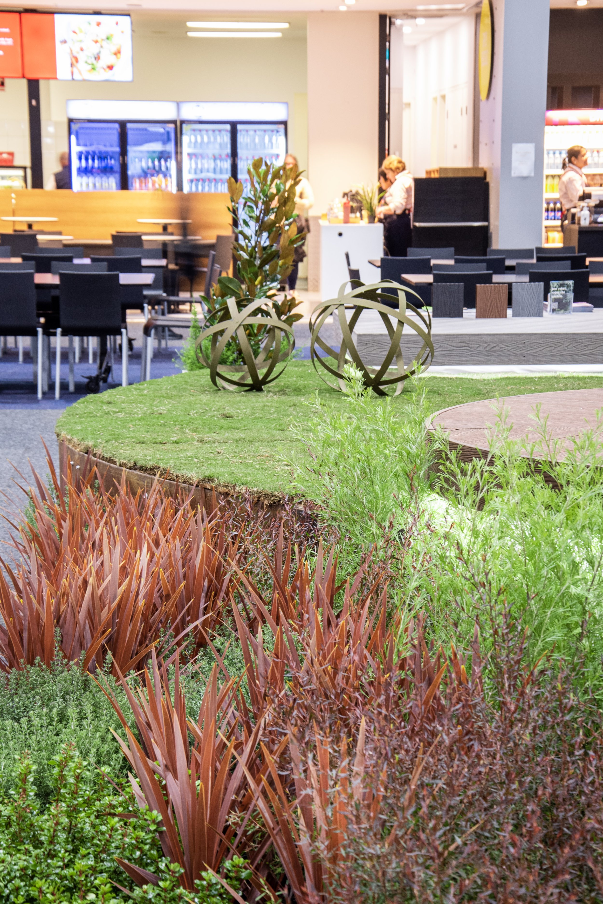 Drift planted vegetation in green and brown, matching with the timber seatings and the modern geometric sculptures.