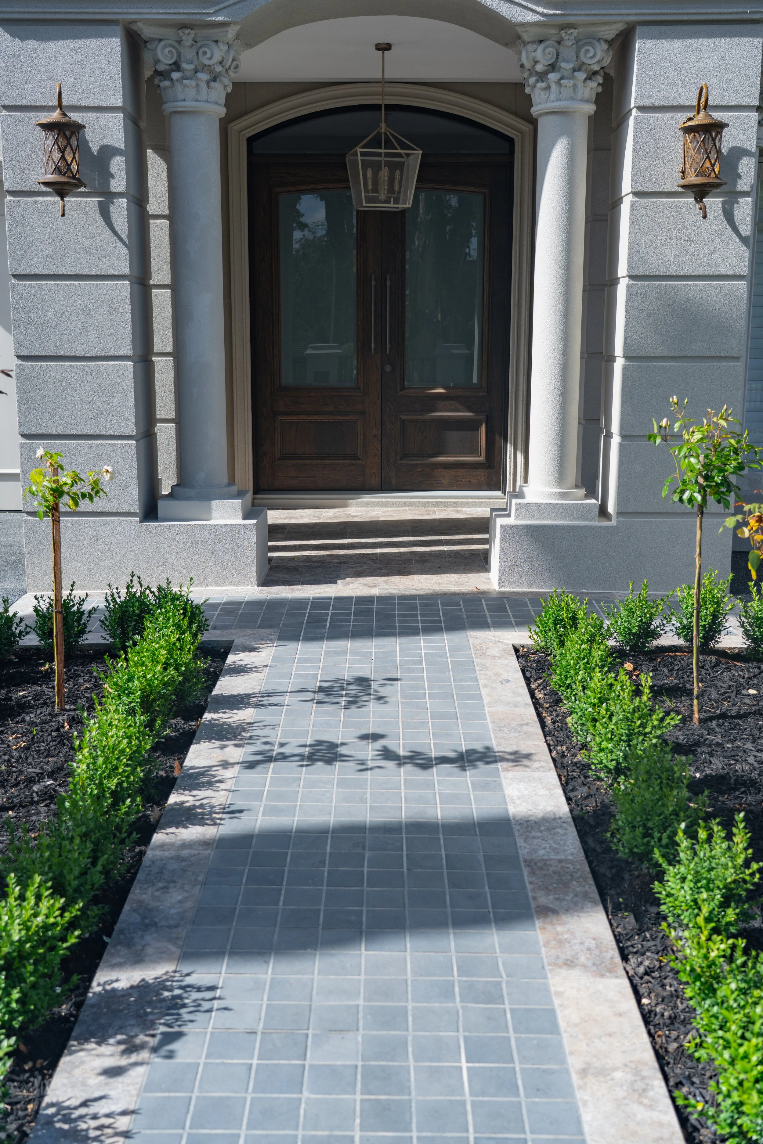 A modern french architecture front porch, with a elegant entrance path with tile bluestone cobble-tiled paving framed with travertine tiling.