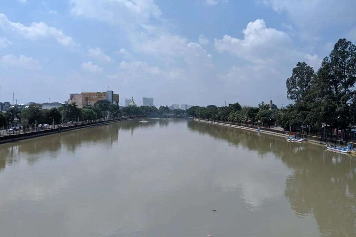 A river lined with trees and buildings on both sides under a partly cloudy sky.