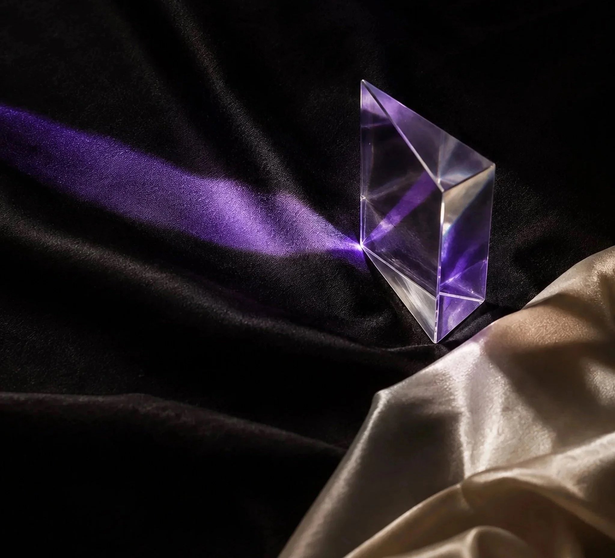 A clear, purple-tinted glass pyramid sculpture on a black fabric background with purple light reflections.