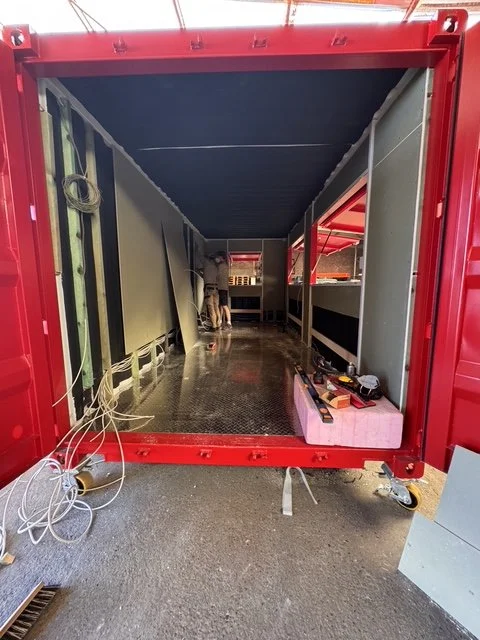 Innenansicht eines leeren, rot lackierten Transportcontainers mit Werkzeugen und Kabel auf dem Boden.