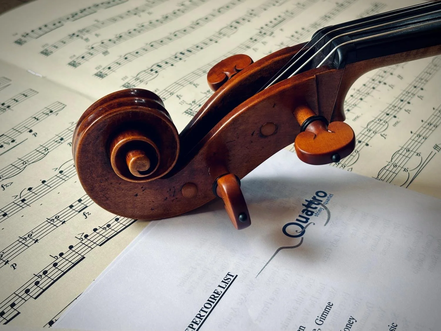 Close-up of a wooden violin scroll resting on sheet music and a Quattro string quartet sheet music.