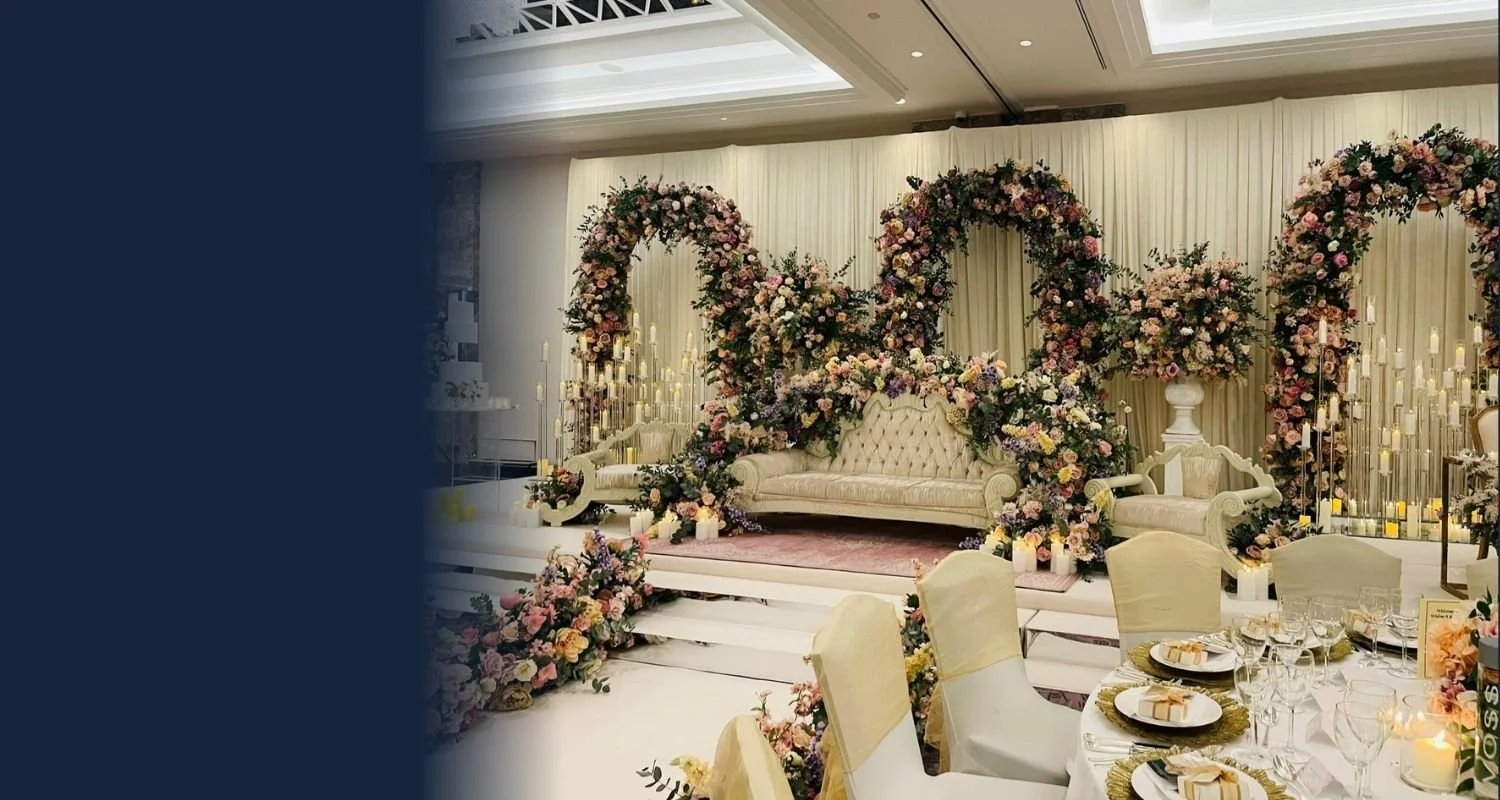 Elegant wedding reception with a decorated stage featuring floral arches, candles, and a vintage cream-colored sofa, surrounded by tables set for guests in a luxurious indoor venue.