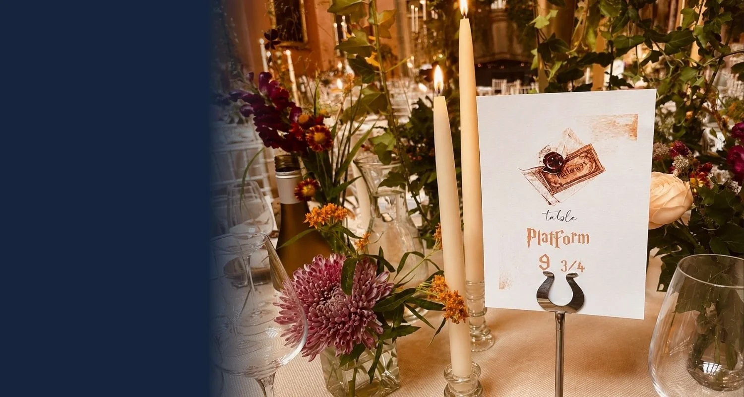 Elegant wedding reception table with floral centerpieces, tall candles, and a table number sign reading 'Table Platform 9 3/4' with a Harry Potter theme.