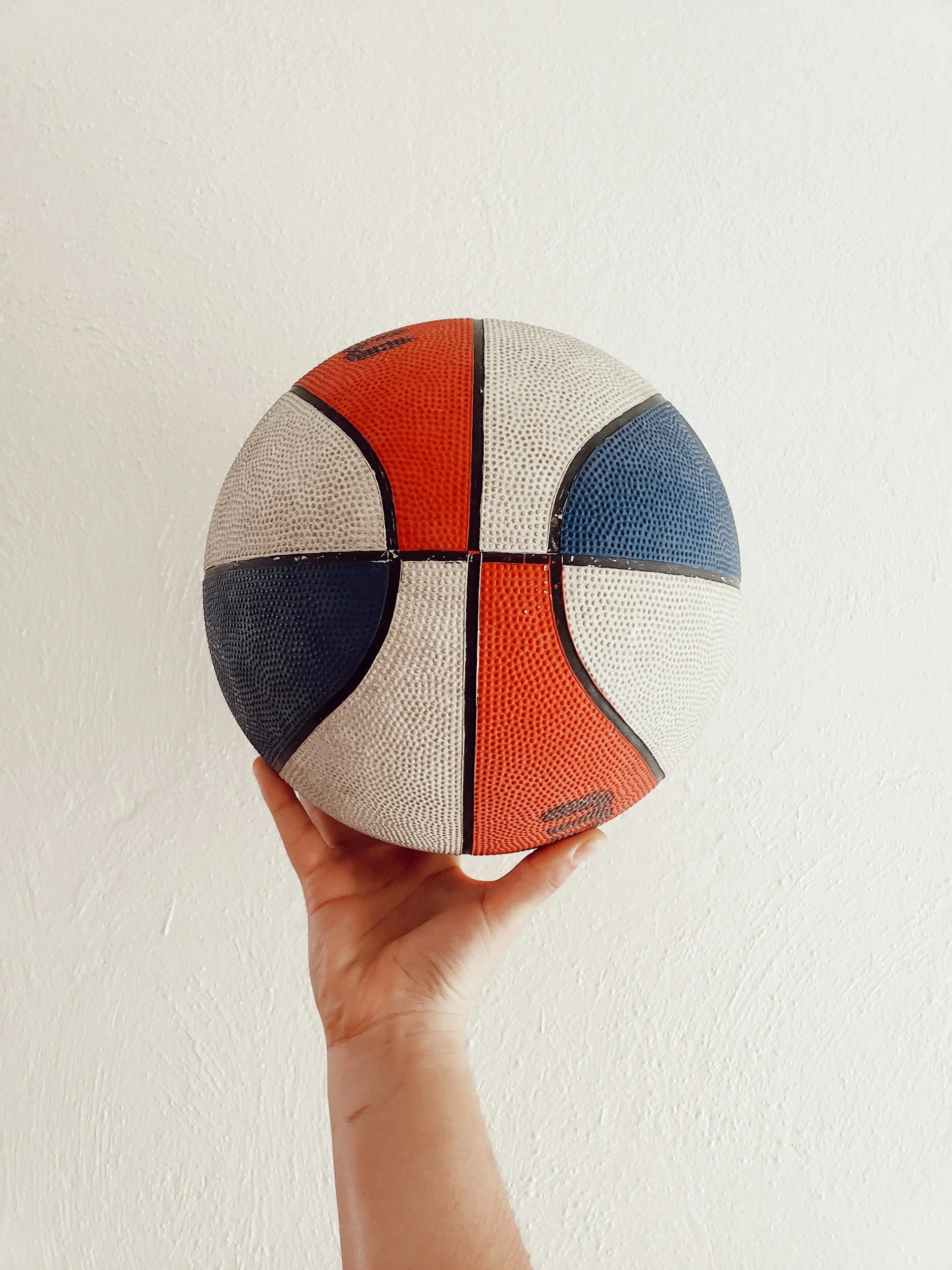 Person holding a multicolored textured basketball against a plain white wall.