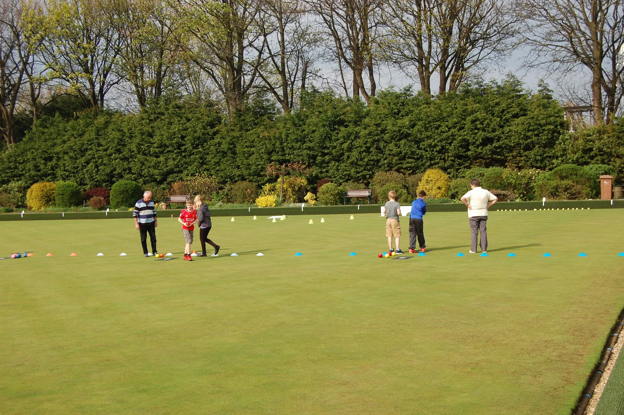 People playing bowling on a green field with trees in the background.