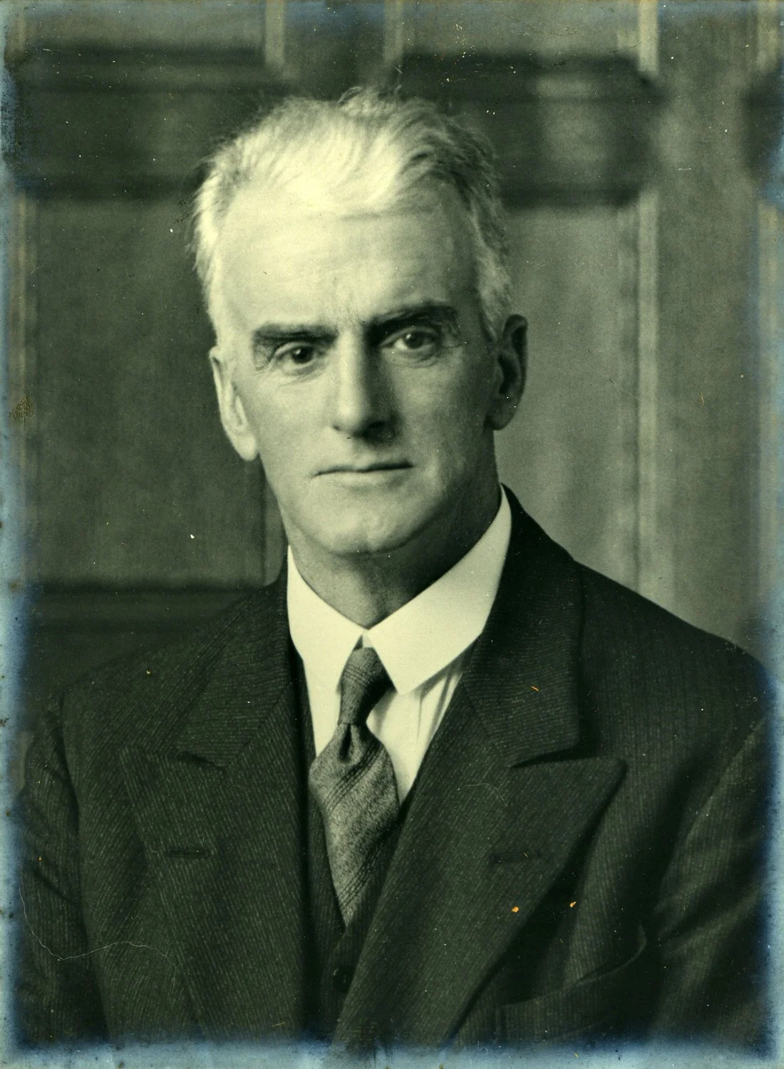 Black and white portrait of a man with white hair wearing a suit and tie.