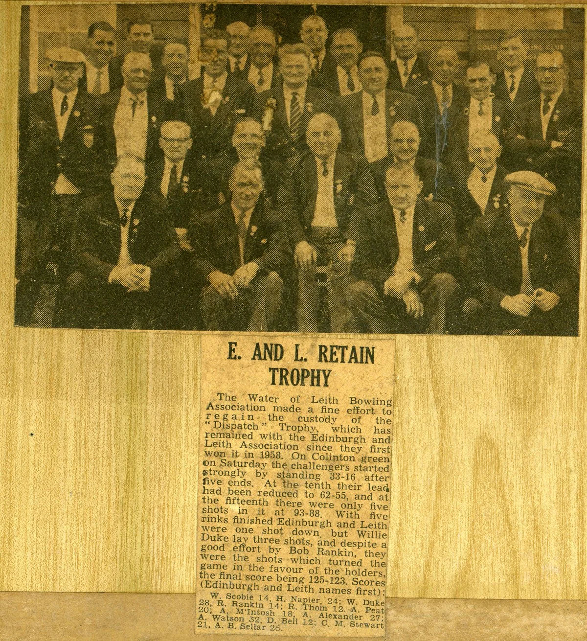 Group of men in suits posing together for a group photo at a bowling event, with a newspaper article below reporting on the event and trophy details.
