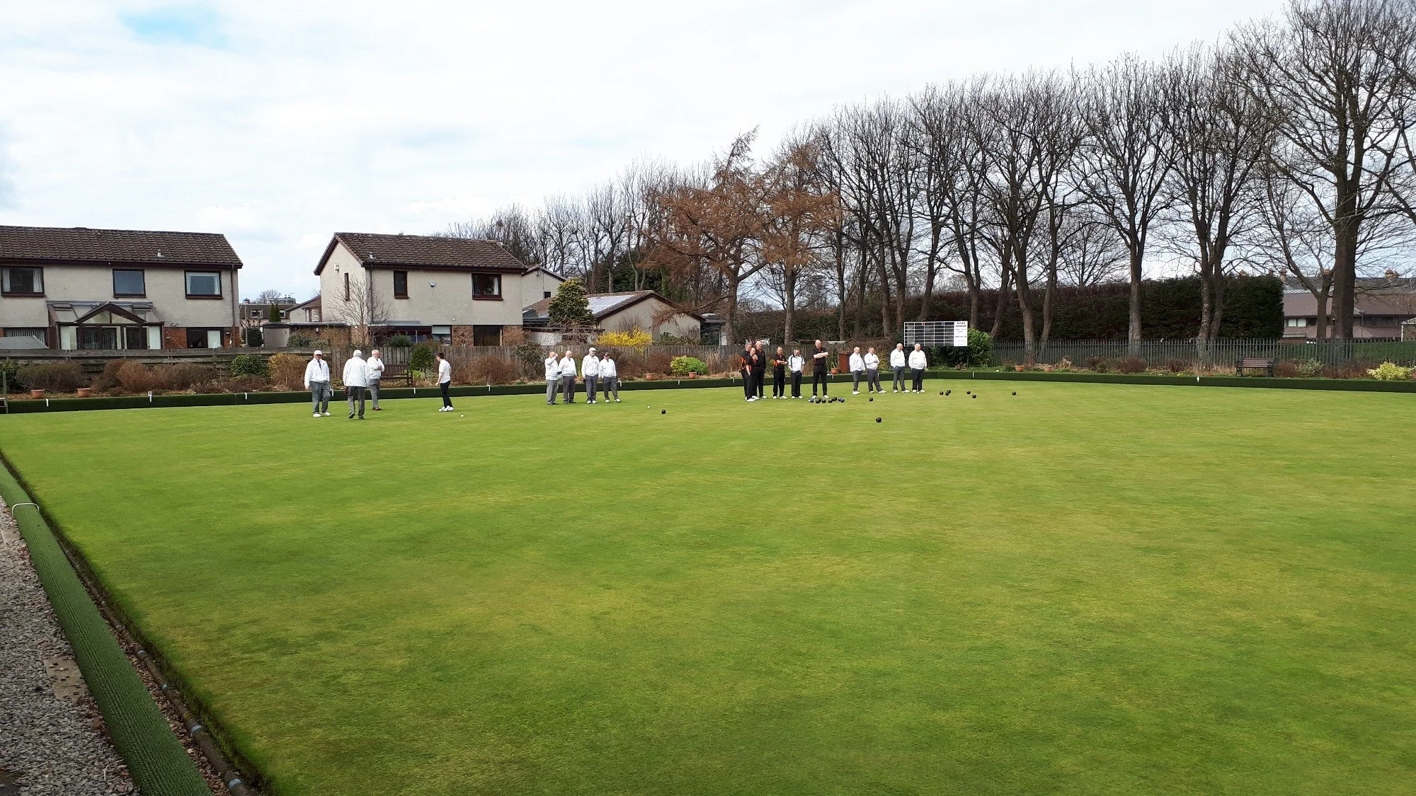 People playing lawn bowls on a green field with houses and trees in the background.