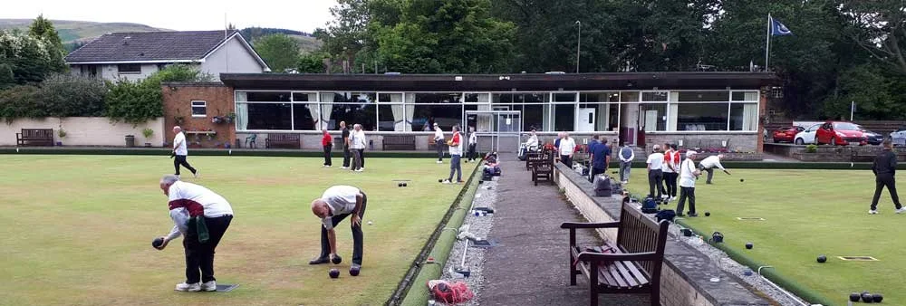 Lawn bowling players on a green field practicing and playing, with a clubhouse in the background.