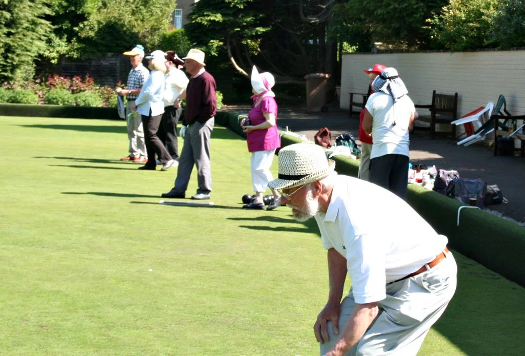 People standing on a lawn playing lawn bowls on a sunny day.