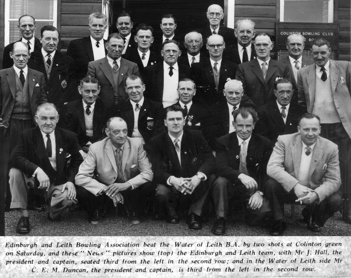 A black-and-white photograph of a group of men posing outside, in front of a building labeled "Colinton Bowling Club." The men are dressed in suits and ties, with some wearing badges or medals. They are arranged in four rows, with the front row seate