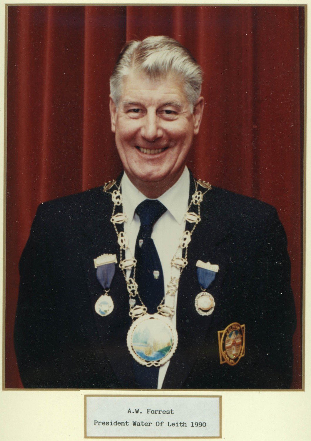 A man smiling in a suit with a chain of office and medals, standing in front of a red curtain. The caption reads 'A.W. Forrest, President Water of Leith 1990.'