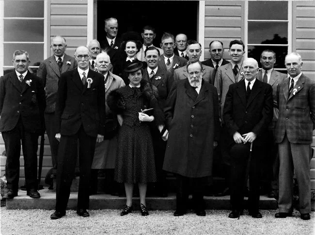 A group of men and women dressed in formal clothing standing outside a building, posing for a photograph.