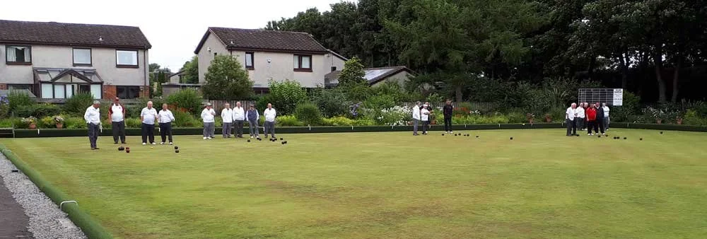 People playing lawn bowls on a grass field, with houses and trees in the background.