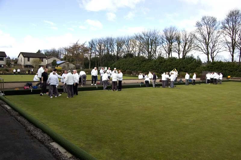 People gathered around a lawn bowling green in a park or recreational area.