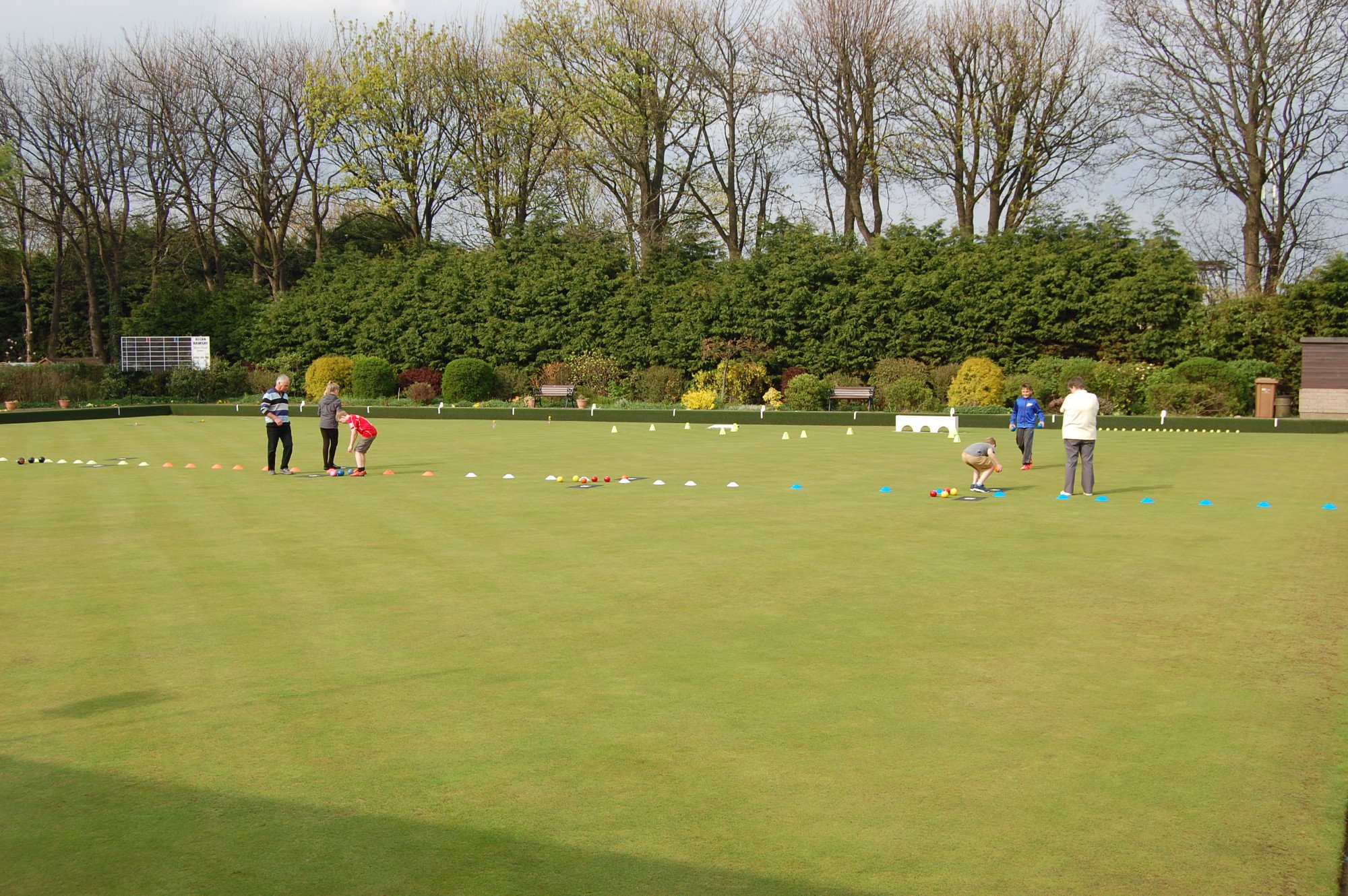 People playing lawn bowls on a green outdoor field with trees and bushes in the background.