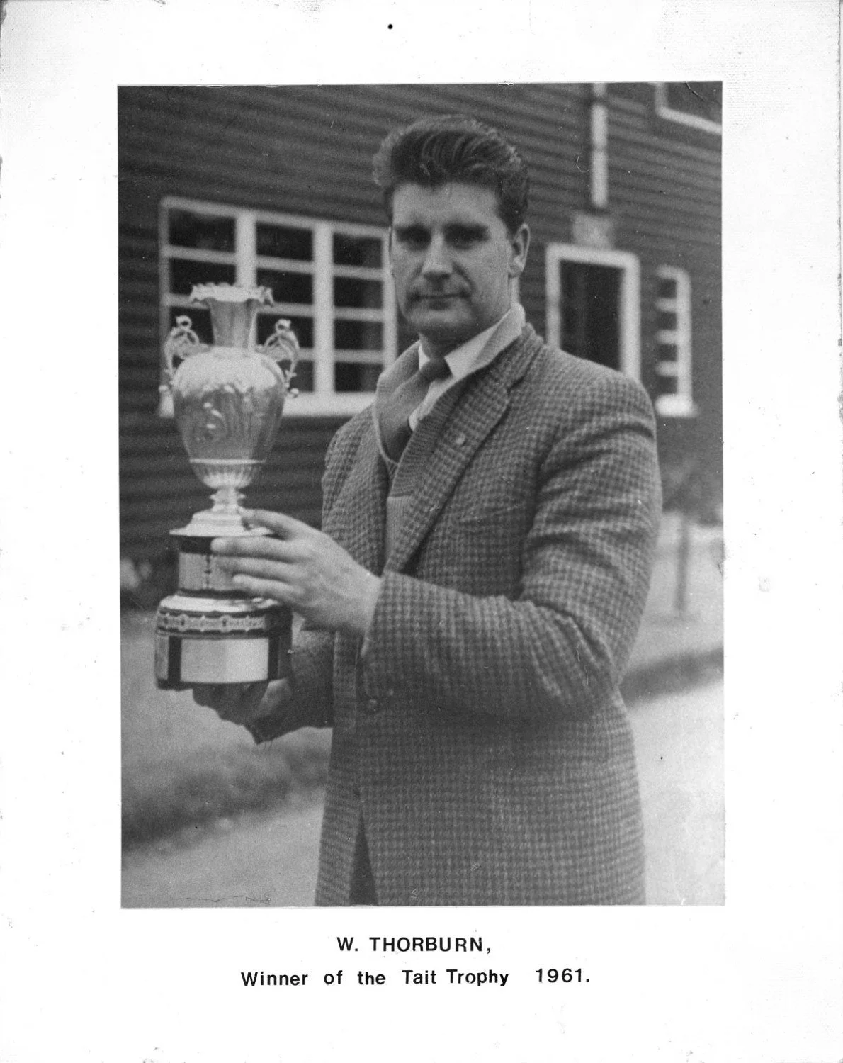 Black and white photo of a man in a checkered jacket holding a trophy, with a building in the background. Text below identifies him as W. Thorburn, winner of the Tait Trophy in 1961.