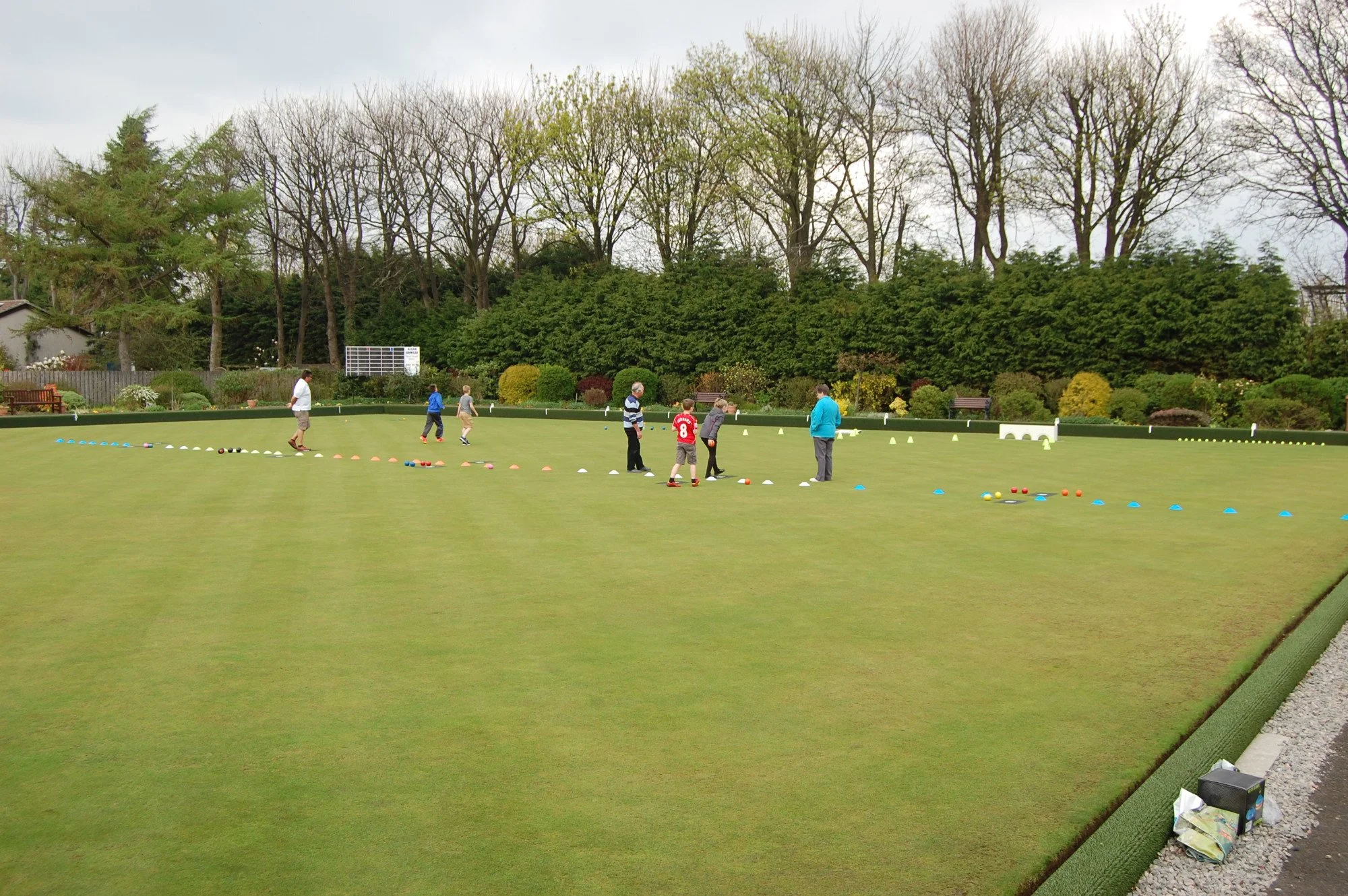 People practicing lawn bowls on a green, with trees and bushes in the background.