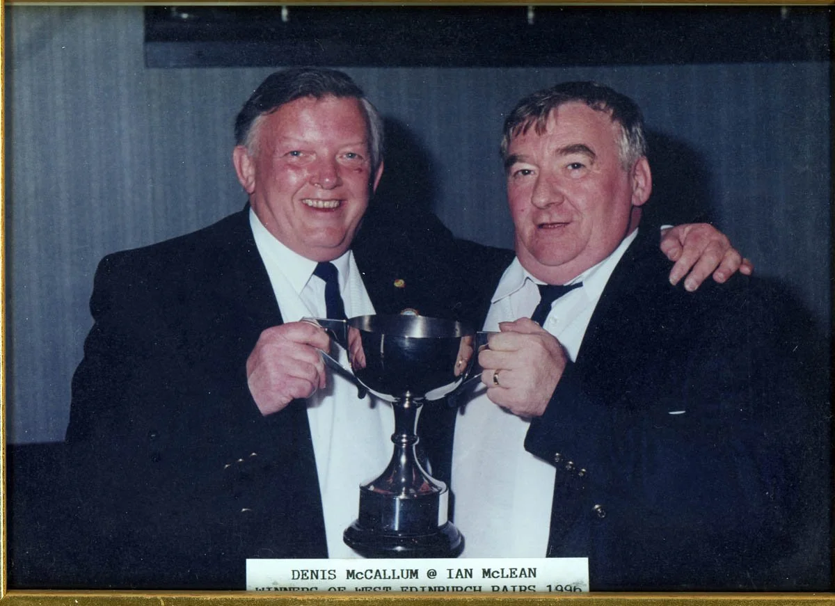 Two men in tuxedos holding a trophy together, smiling for the camera.