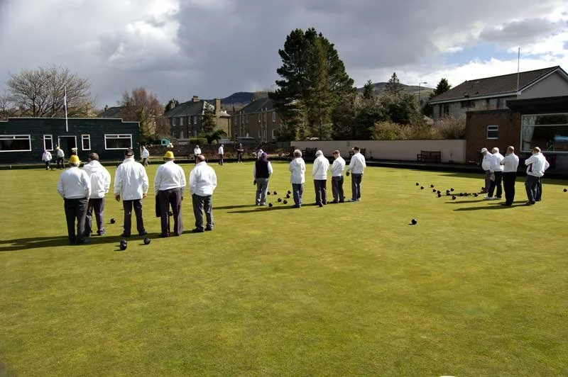 People playing lawn bowls on a well-maintained grass field in a residential neighborhood.