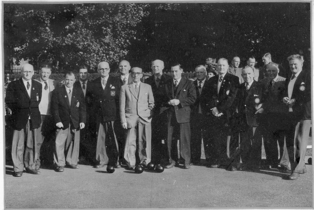 A black and white photo of a group of men standing outdoors, dressed in suits, some with ties and badges, posing for a group picture.