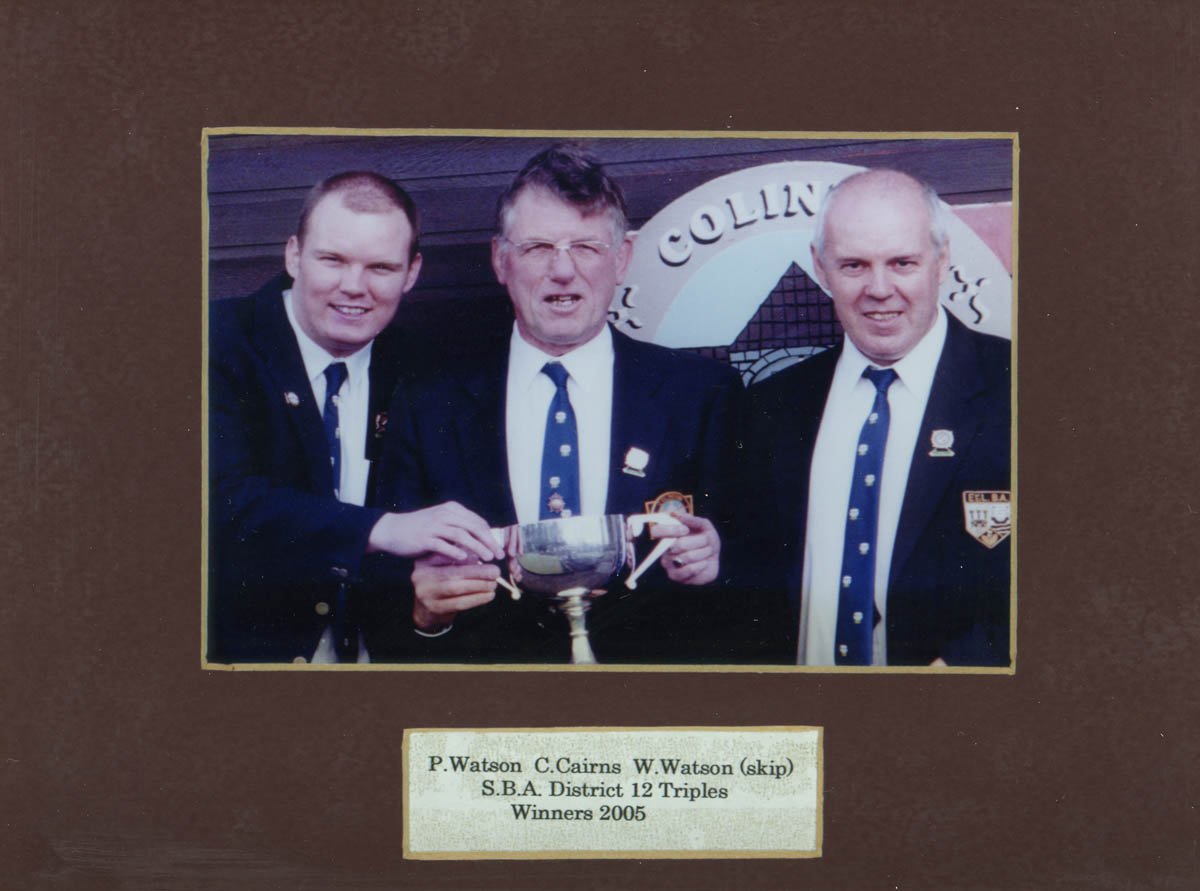 A photo of three men in formal suits and ties, holding a trophy and smiling. They are standing in front of a sign that reads 'Collingwood.' The photo is labeled with names and details of the winners from 2005, indicating they are winners of a trophy 