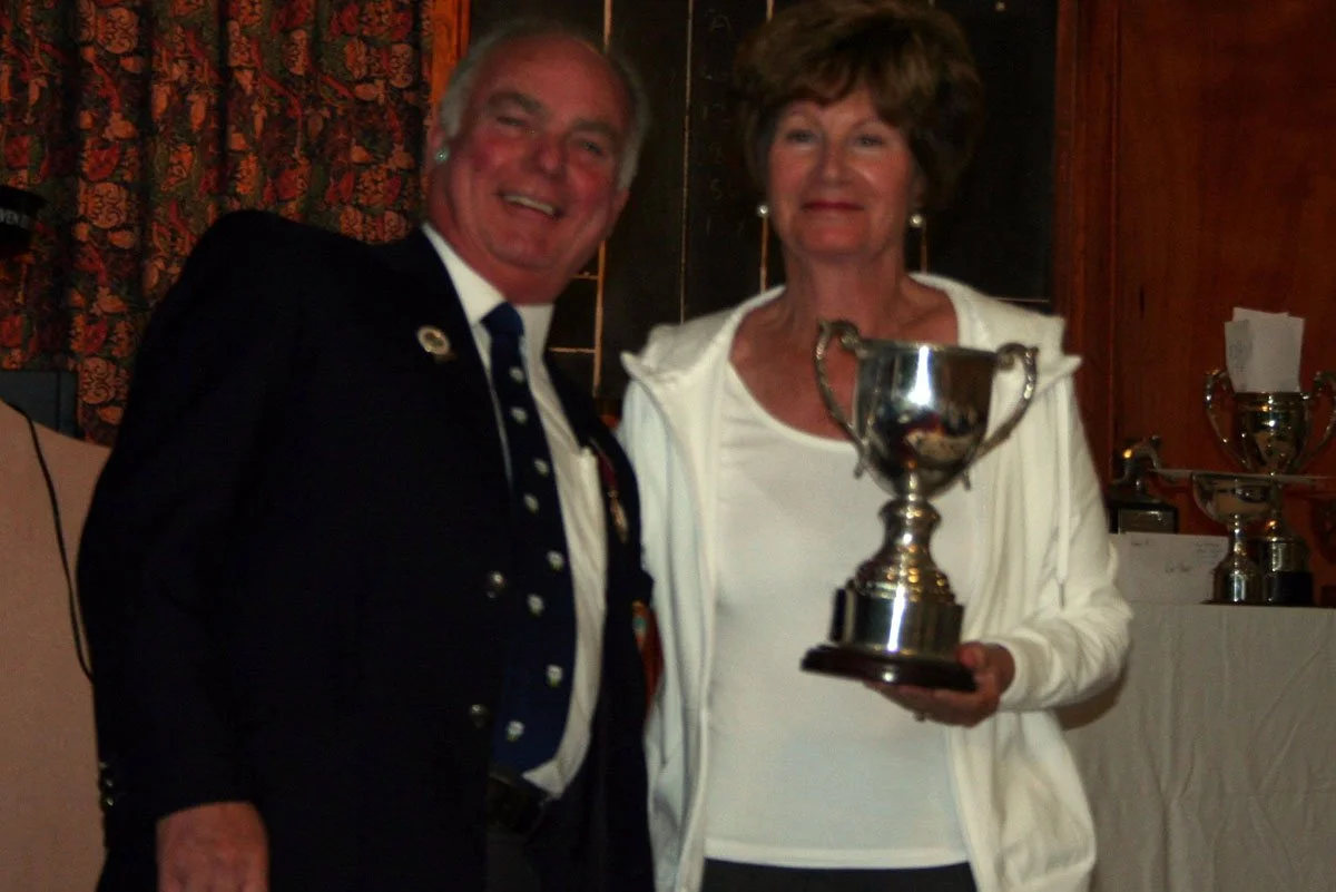 A man in a dark blazer and a woman in a white jacket holding a silver trophy at an award ceremony