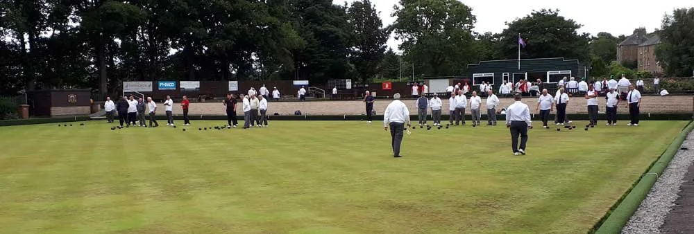 A group of people gathered on a bowling green, playing or watching lawn bowls.
