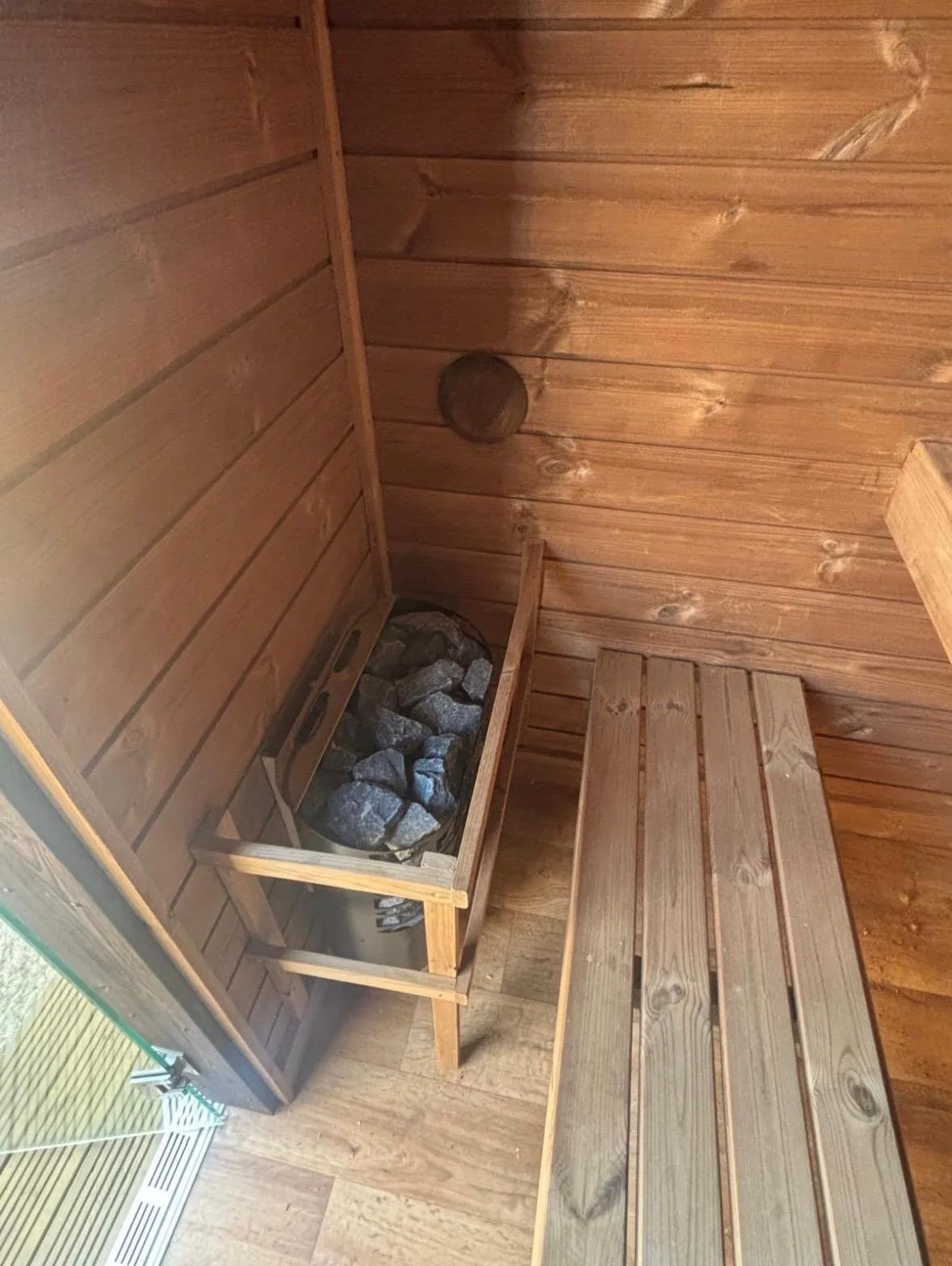Inside a wooden sauna room with a heater filled with rocks and a wooden bench.