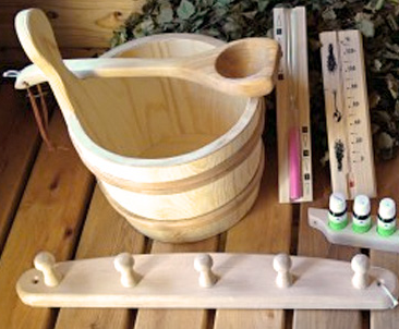 Wooden sauna bucket with a ladle, thermometer, hygrometer, and a wooden backrest or rack on a wooden surface.
