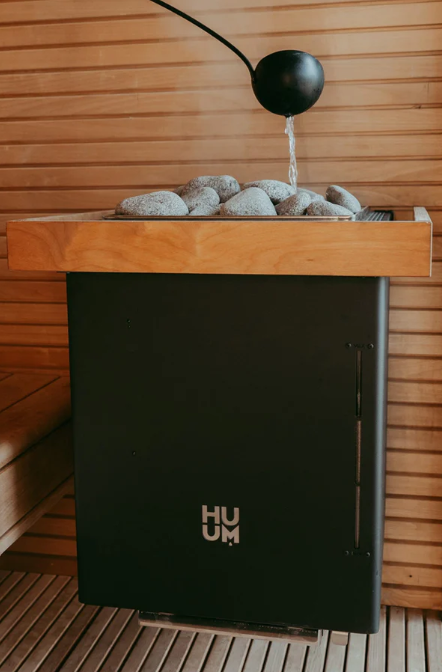 A meditation fountain with a black sphere water feature pouring water onto a bed of rocks, set inside a room with wooden walls and flooring.