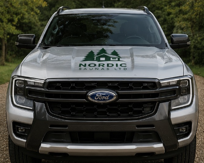 Front view of a silver Ford truck with a Nordic Saunas LTD logo on the hood, parked outdoors with greenery in the background.