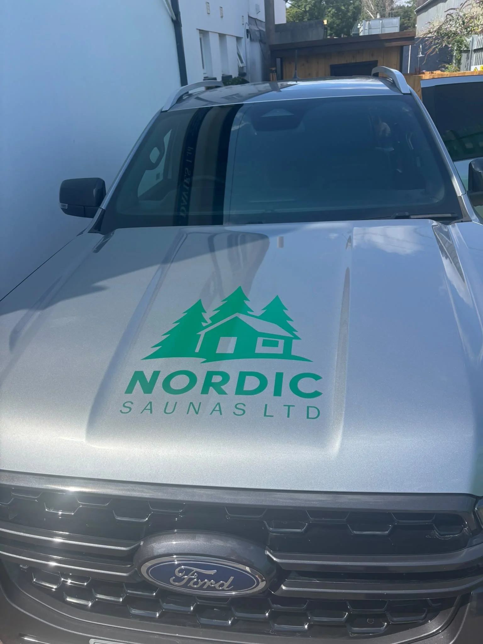 The front of a Ford vehicle with a sticker on the hood that reads 'Nordic Saunas Ltd' and a logo featuring green pine trees and a small house.