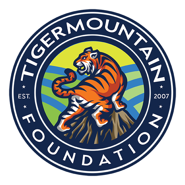 Logo of the Tiger Mountain Foundation featuring a tiger standing on rocks with a background of green and blue stripes, the foundation's name, and the year 2007.