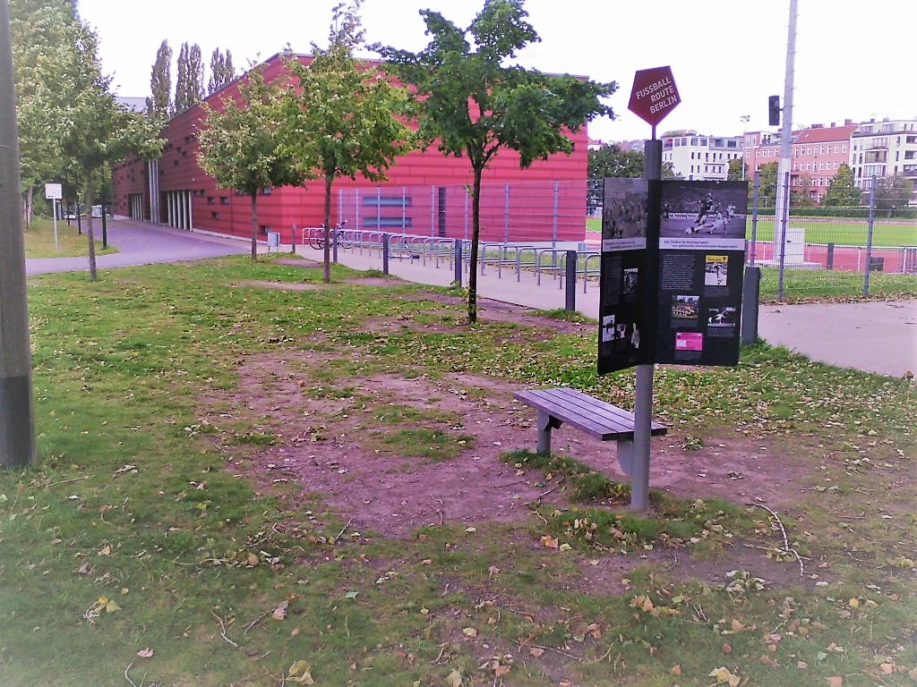 Dit bankje is het verzamelpunt. Op de achtergrond zie je het kleine stadion (met loopbanen voor hardlopers). In het kleine stadion zijn tevens toiletten waar we kosteloos gebruik van kunnen maken.