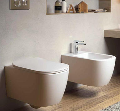 Modern bathroom with a wall-mounted toilet and a bidet, light-colored wall, wooden flooring, and a floating shelf with bathroom items.