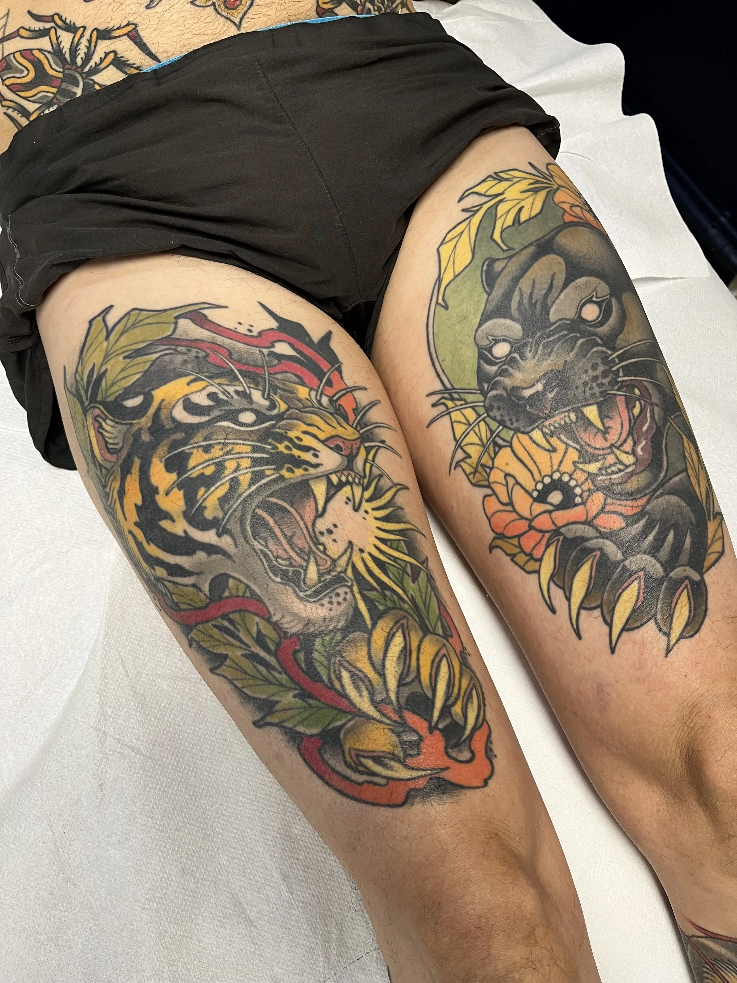 Tatouage de deux félins agressifs,, un sur chaque cuisse, entourés de feuilles jaunes, oranges et vertes.