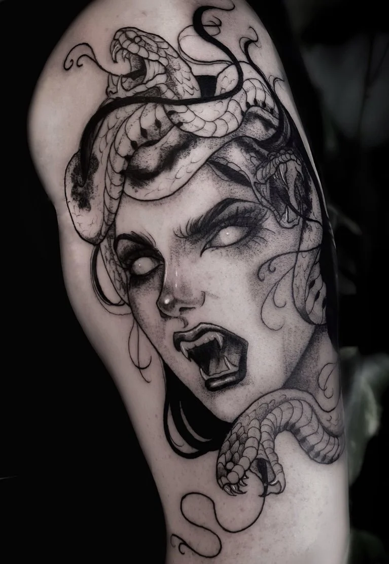 Tatouage en noir et gris d'une Médusa au visage expressif avec cheveux sombres, bouche ouverte montrant des dents pointues, et un serpent enroulé autour de sa tête.