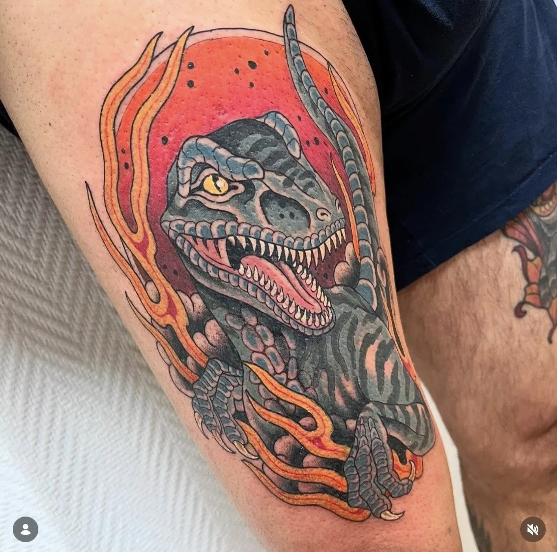 Tatouage d'un dinosaure genre tyrannosaure, entouré de flammes orange et rouges.