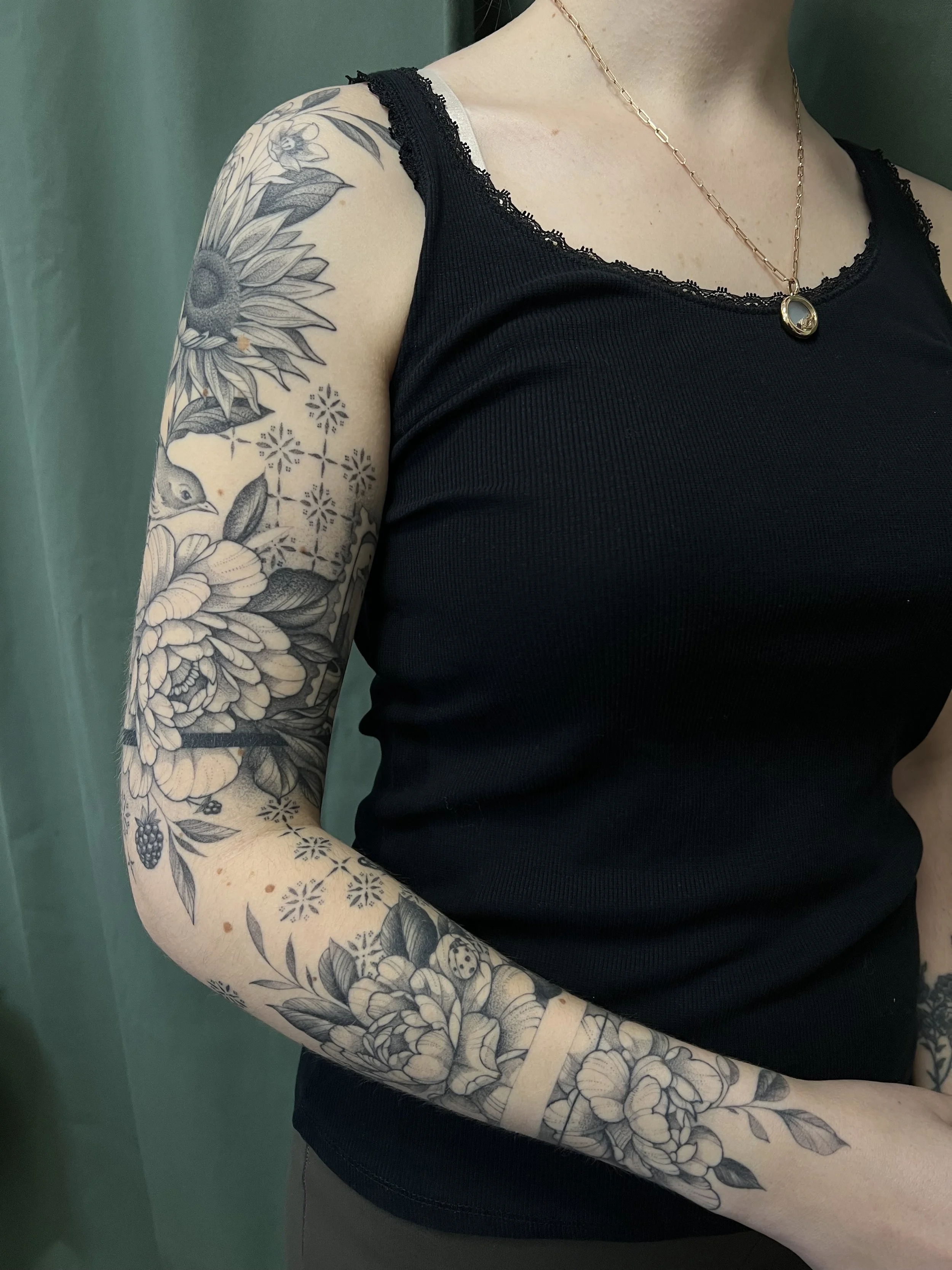 Un bras d'une personne avec un tatouage détaillé de fleurs, de feuilles et d'un oiseau avec des motifs géométriques.