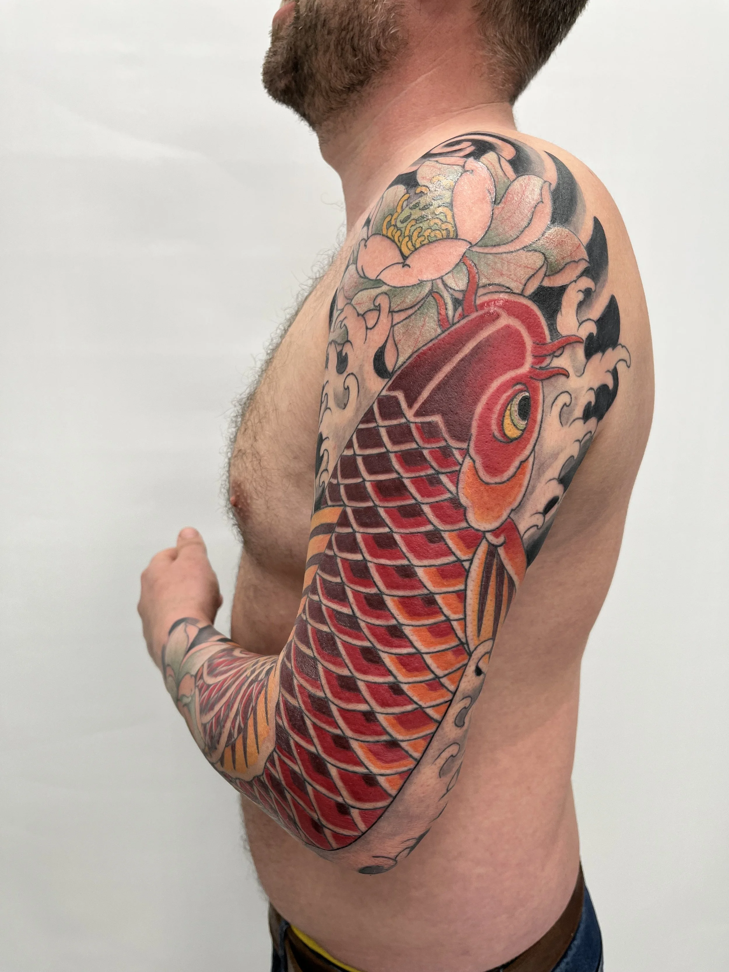 Tatouage de carpe koi aux couleurs rouge, orange et jaune couvrant le bras et l'épaule d'un homme.