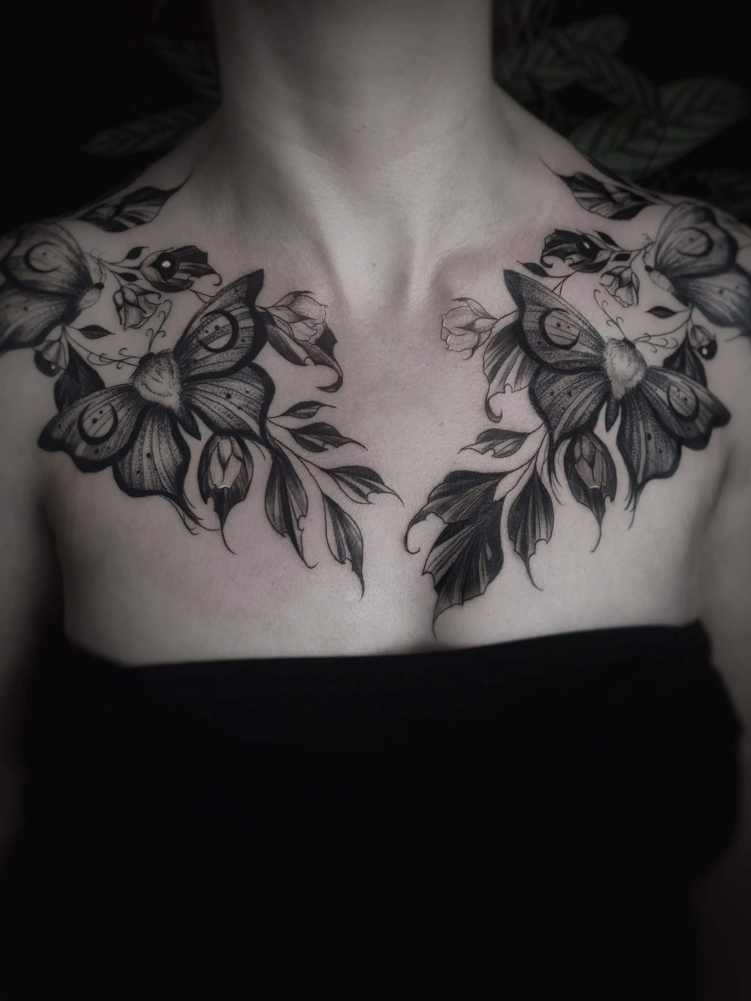 Un tatouage noir et gris représentant deux papillons et des fleurs sur le haut de la poitrine d'une personne
