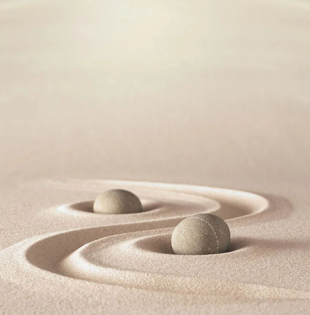 Two round stones on a smooth sand surface, with ripples around them, creating a minimalist, Zen-like scene.