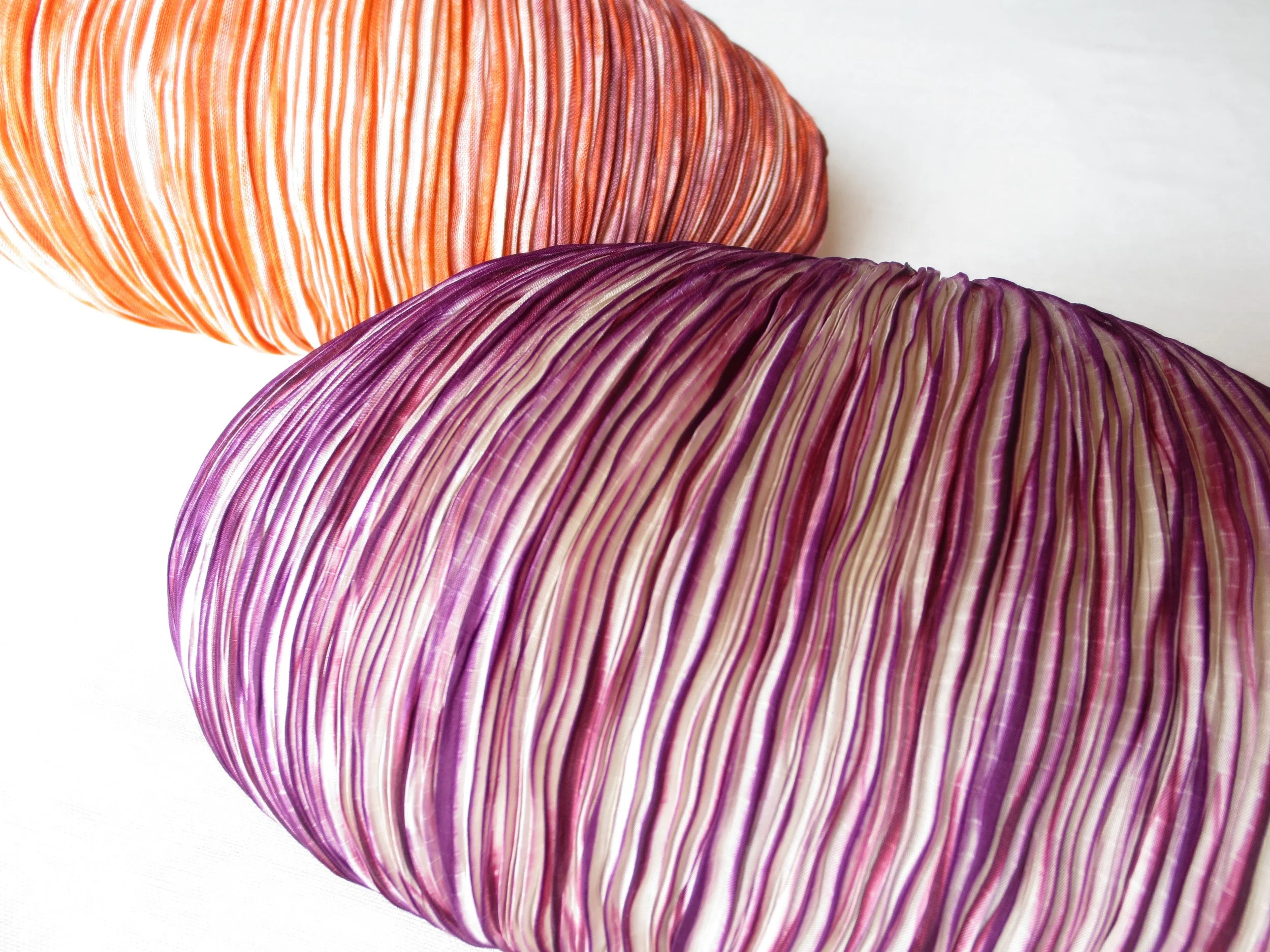 Tessuto realizzato con tecnica shibori con linee di diversi colori, una arancione e una viola, su sfondo bianco.