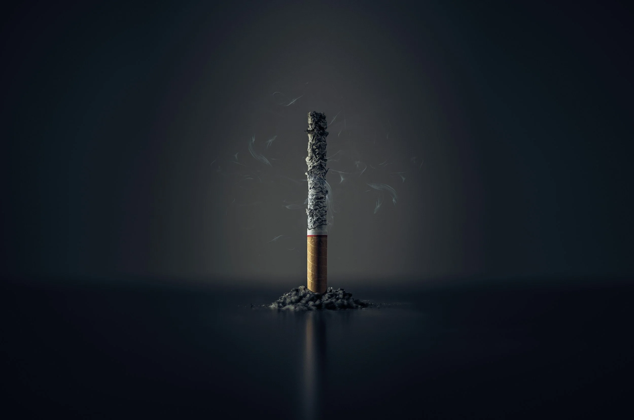 Cigarette éteinte sur une surface sombre, avec de la cendre et des étincelles ou flammes faibles qui s'en échappent.