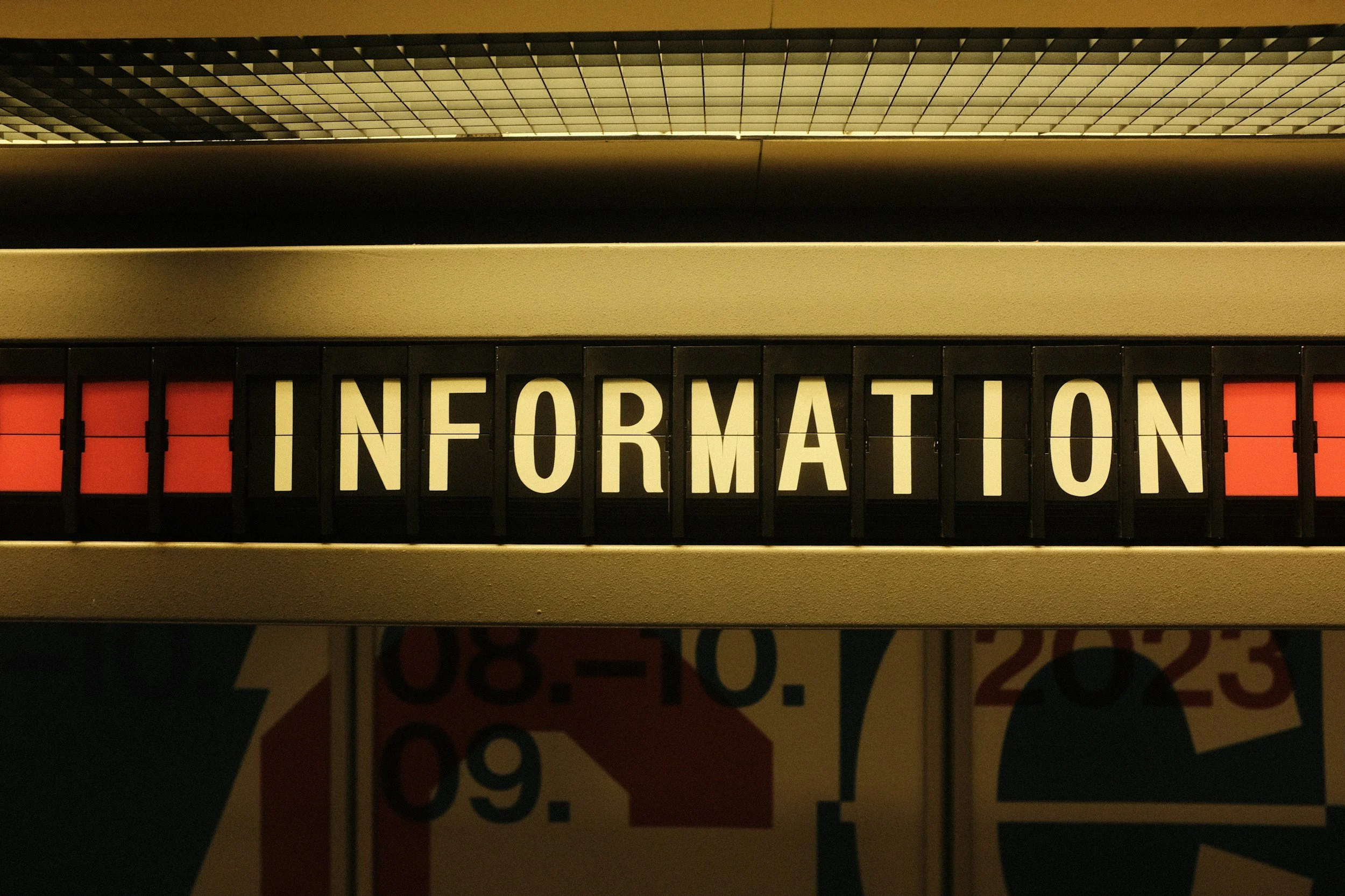 Un panneau lumineux avec le mot 'INFORMATION' écrit en lettres blanches sur fond noir, situé dans un environnement intérieur.