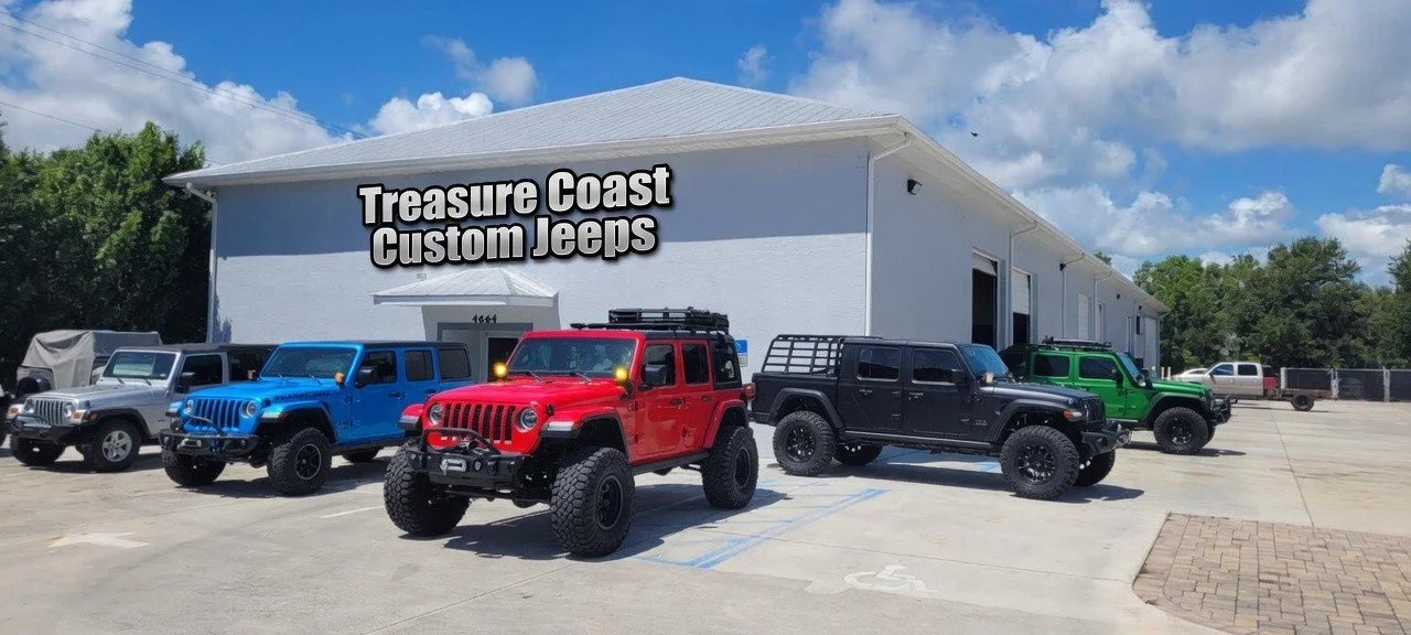 Multiple Jeep vehicles parked in front of a dealership with a sign that reads 'Treasure Coast Custom Jeeps.'