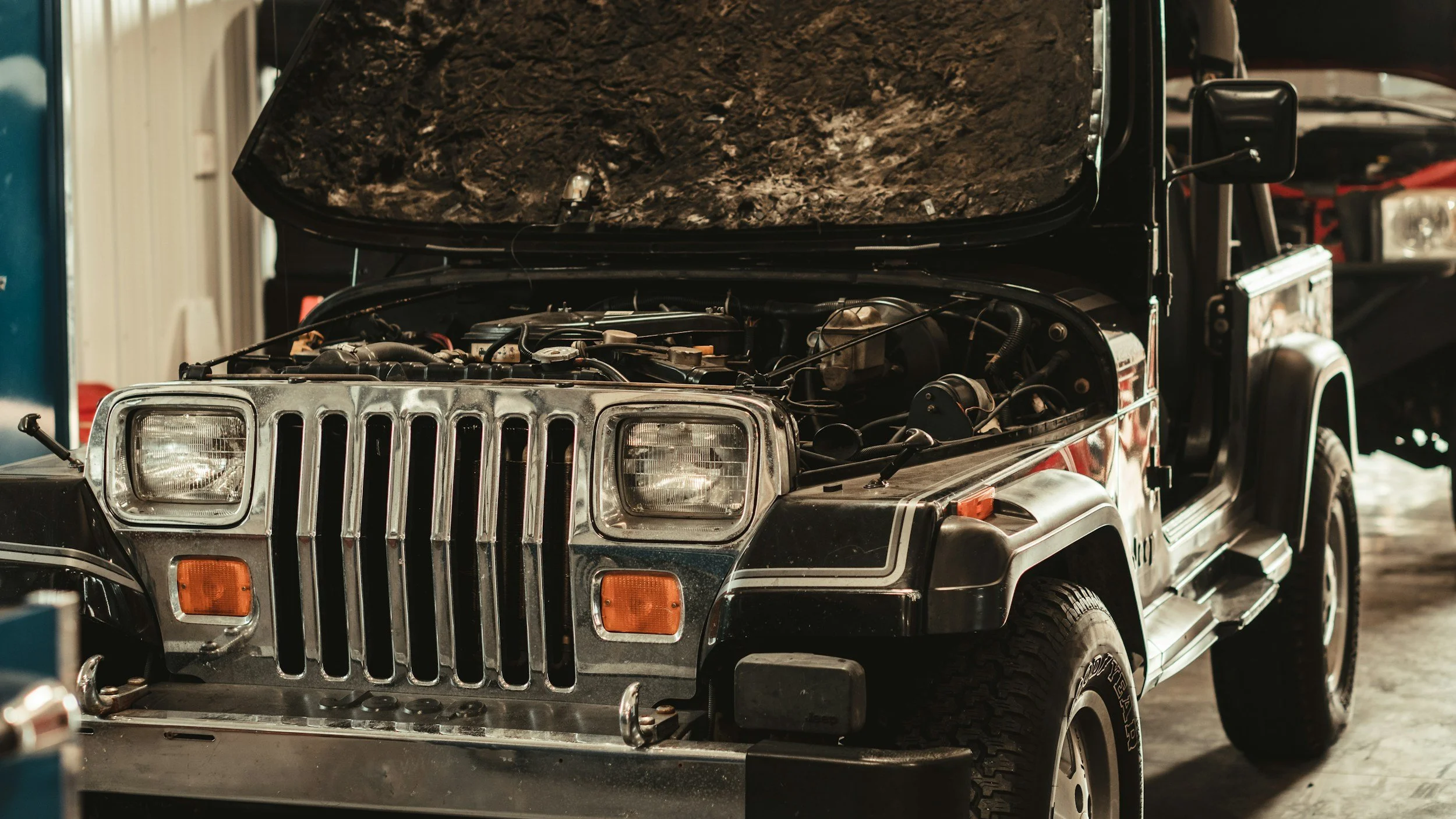 A black Jeep with its hood open inside a garage, showing the engine and other mechanical parts.