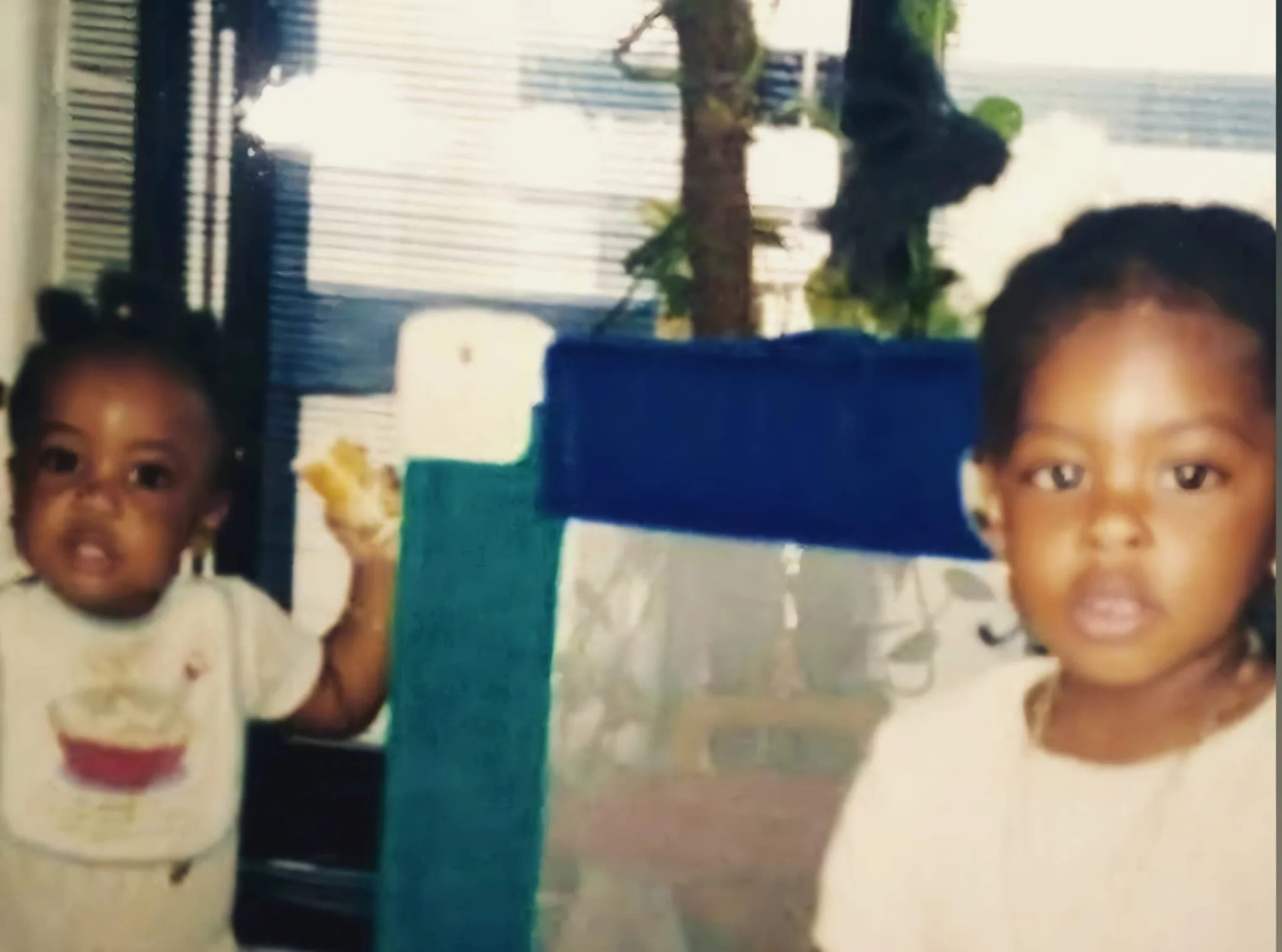 Two young children wearing white shirts, with blurred background suggesting an indoor setting.